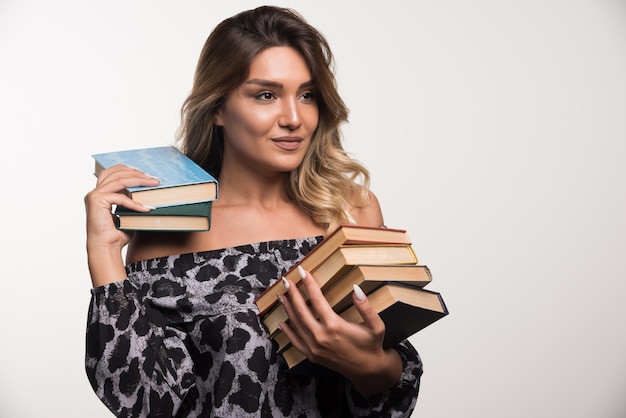 Young woman holding books while looking aside on white wall.