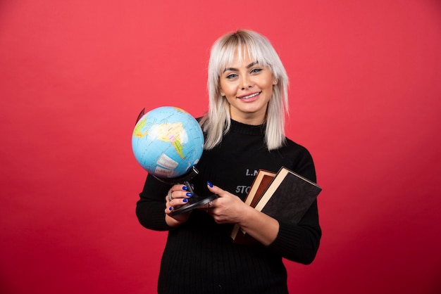 Free photo young woman holding books with earth globe and smiling