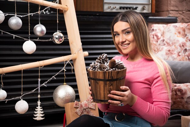 Young woman holding bucket of pinecones at home.