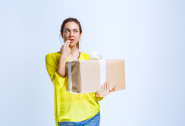 Young woman holding a cardboard gift box and thinking about the unknown sender