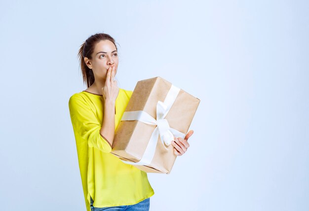 Young woman holding a cardboard gift box and thinking about the unknown sender