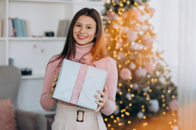 Young woman holding christmas present by christmas tree