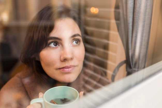 Young woman holding a cup of coffee while being covered with a blanket