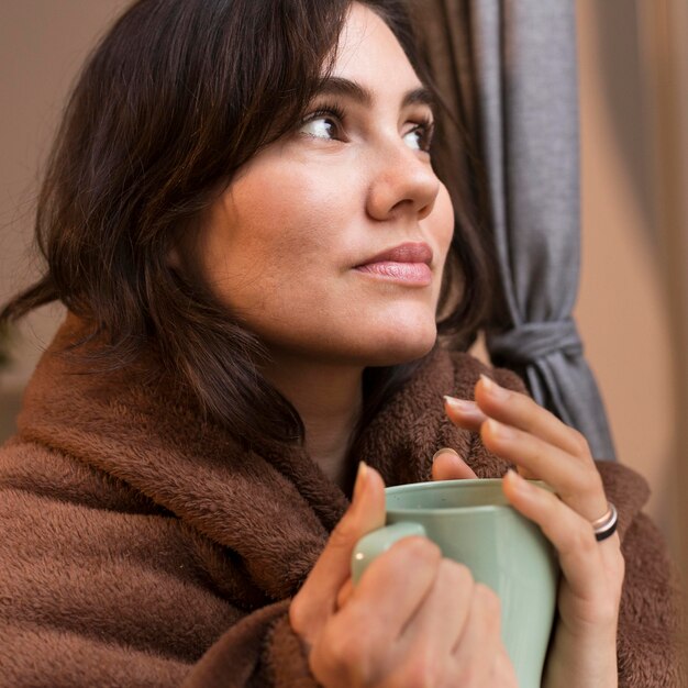 Young woman holding a cup of coffee while being covered with a blanket