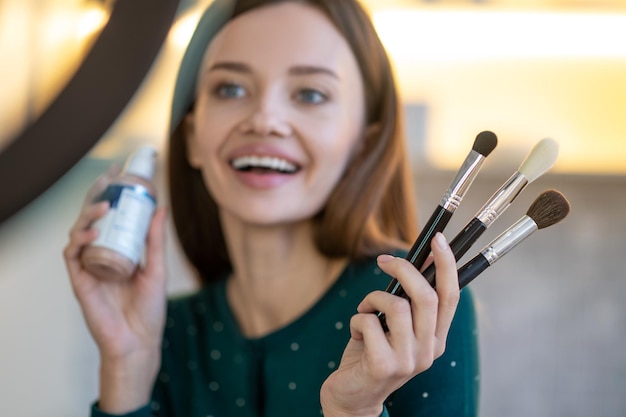 Young woman holding face brushes and smiling