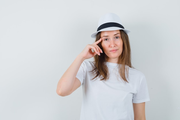 Free Photo young woman holding finger on temples in white t-shirt, hat and looking sensible.