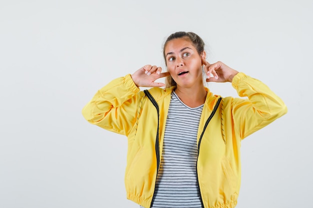 Free photo young woman holding fingers near ears in t-shirt, jacket and looking dreamy , front view.