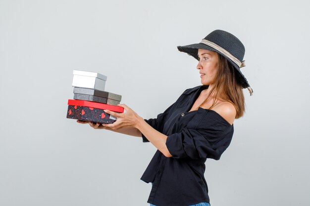 Young woman holding gift boxes in shirt, shorts, hat and looking careful .