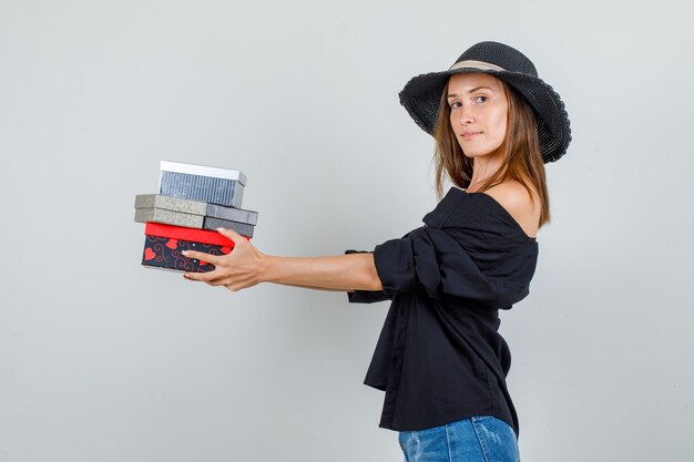 Young woman holding gift boxes and smiling in shirt, shorts, hat .