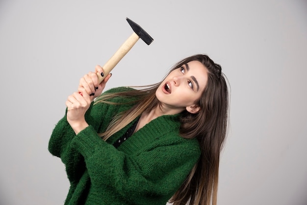 Young woman holding hammer in hands on a gray background.