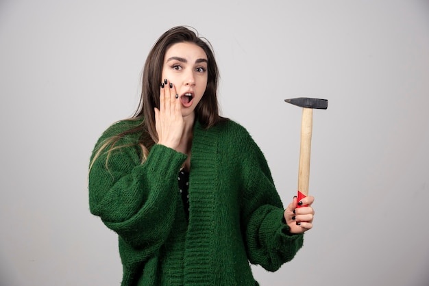 Young woman holding hammer in hands on a gray background.