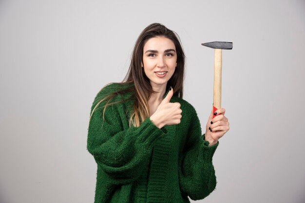 A young woman holding a hammer and showing a thumb up.