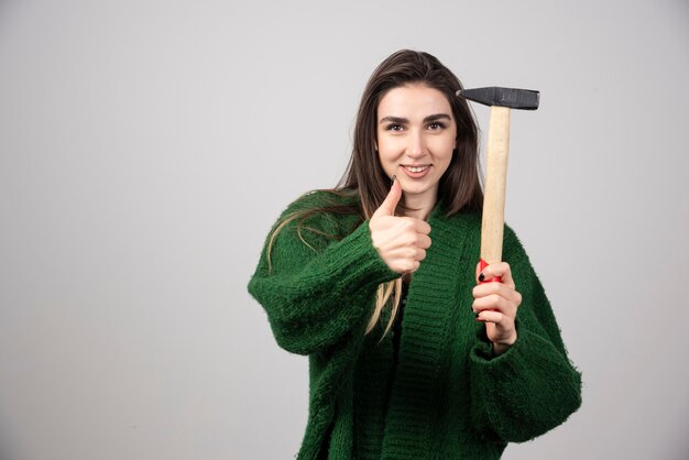 A young woman holding a hammer and showing a thumb up.