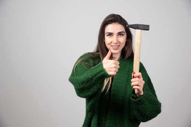 A young woman holding a hammer and showing a thumb up.