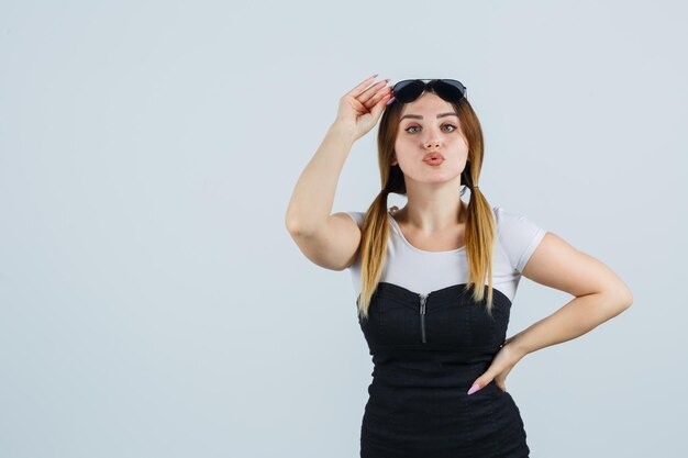 Young woman holding hand on glasses while pouting lips