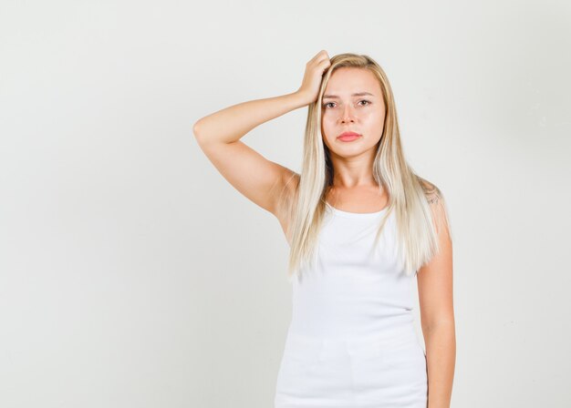 Young woman holding hand on hair in white singlet and looking upset.