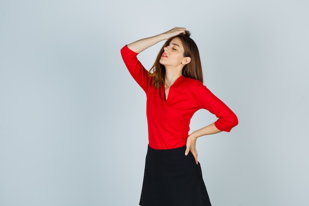 Free Photo young woman holding hand on head, putting hand on hip while posing in red blouse