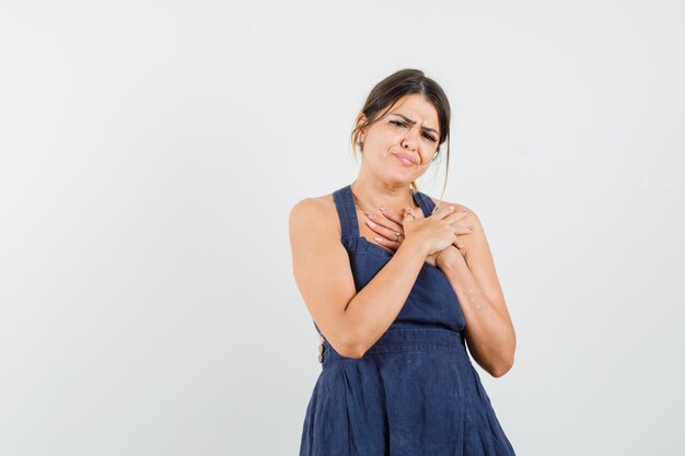 Young woman holding hands on chest in dress and looking painful