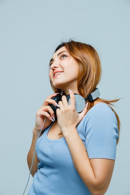 Young woman holding hands on headphones while looking up