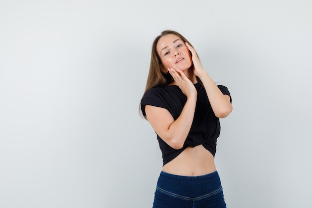 Young woman holding hands on her face in black blouse and looking attractive