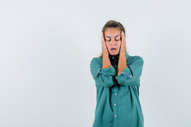 Young woman holding hands on her temples in blue shirt and looking exhausted