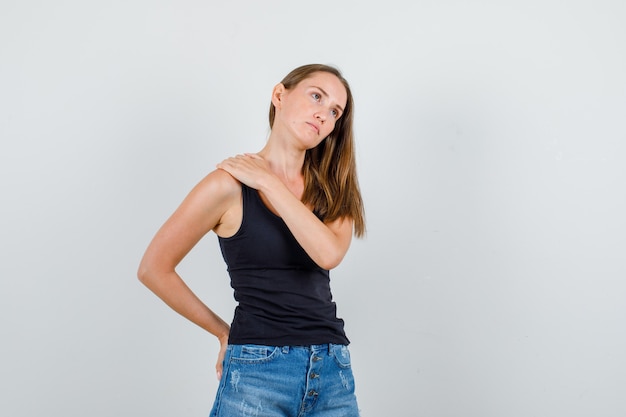 Young woman holding hands on shoulder and back in singlet, shorts and looking sad