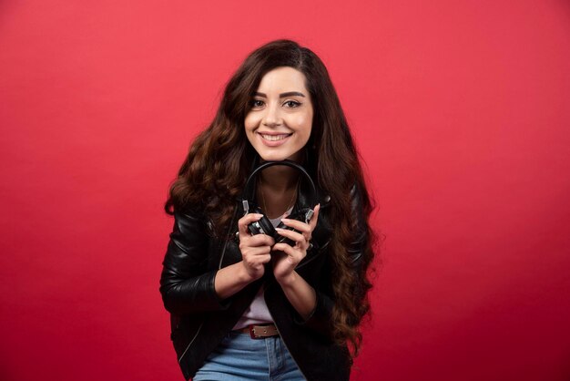 Young woman holding headphones and posing on a red background. High quality photo