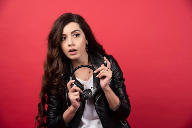 Young woman holding headphones and posing on a red background. High quality photo