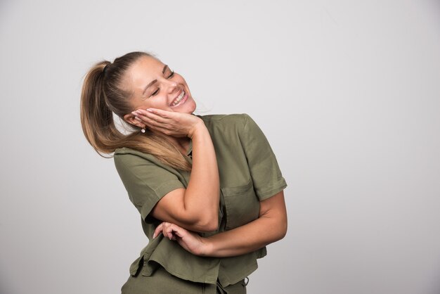 Young woman holding her cheek on gray wall.