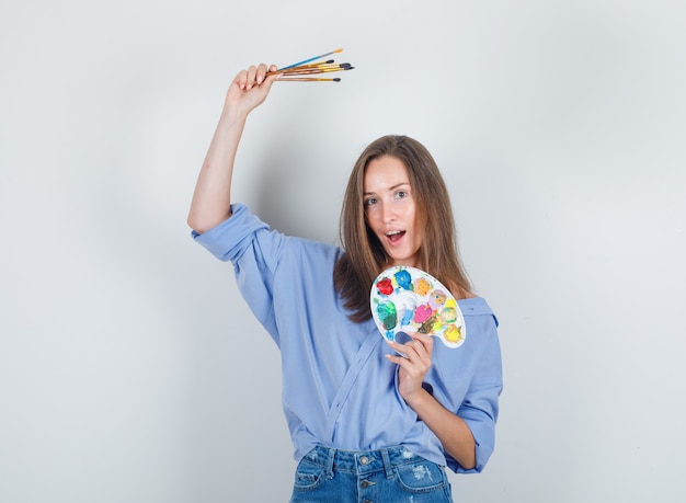 Free photo young woman holding painting tools in blue shirt, shorts and looking happy