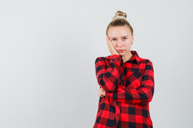 Young woman holding palm on cheek in checked shirt and looking depressed