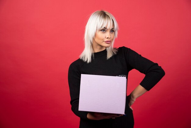 Free Photo young woman holding a present on a red wall. 