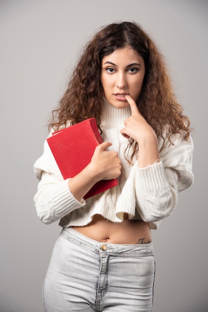 Young woman holding red book on a gray wall. High quality photo