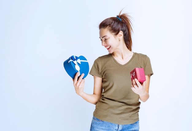 Young woman holding red and heart shape blue gift boxes and enjoying them