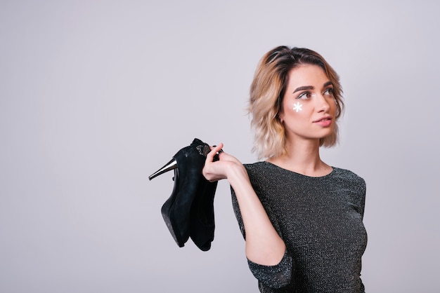 Young woman holding shoes after party