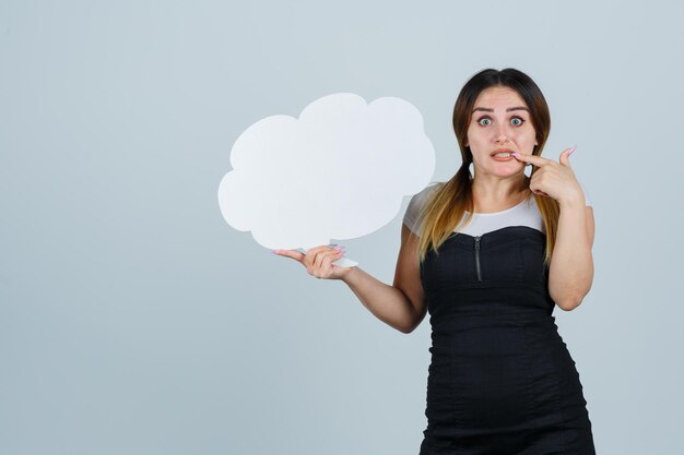 Young woman holding speech bubble while biting her nails