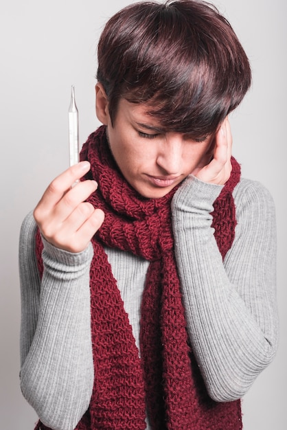 Young woman holding thermometer in hand having headache