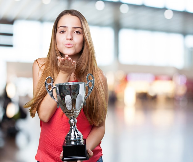 Free photo young woman holding a trophy and sending a kiss on a white backg