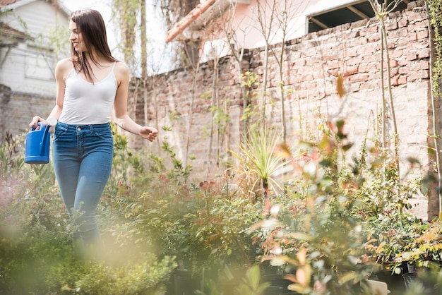 Free photo young woman holding watering can standing between the growing plants