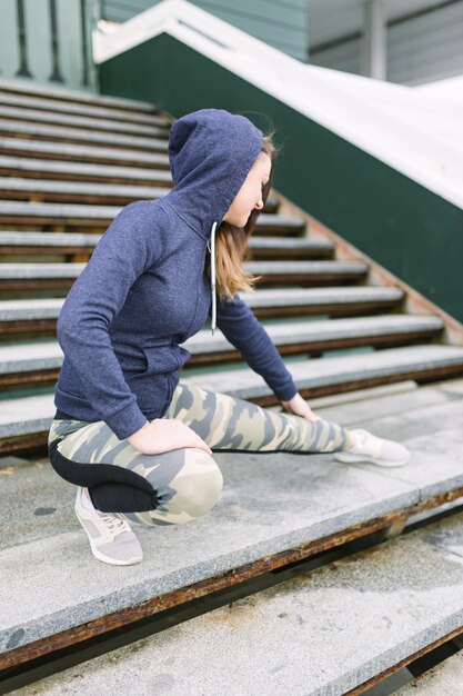 Young woman in hooded top stretching her leg on staircase