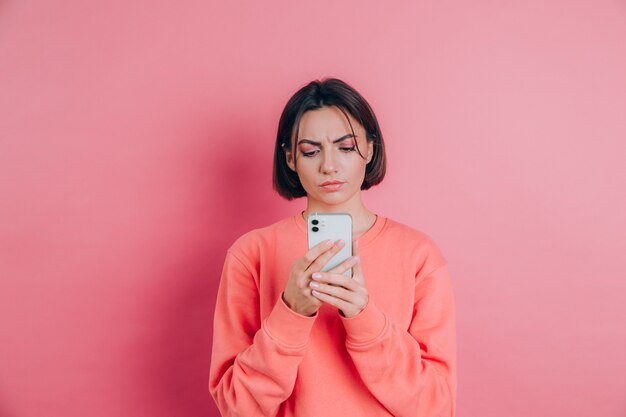 Young woman is feeling sad unhappy angry while reading sms using her mobile phone, over pink background