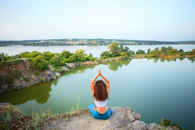 Free photo young woman is practicing yoga near river