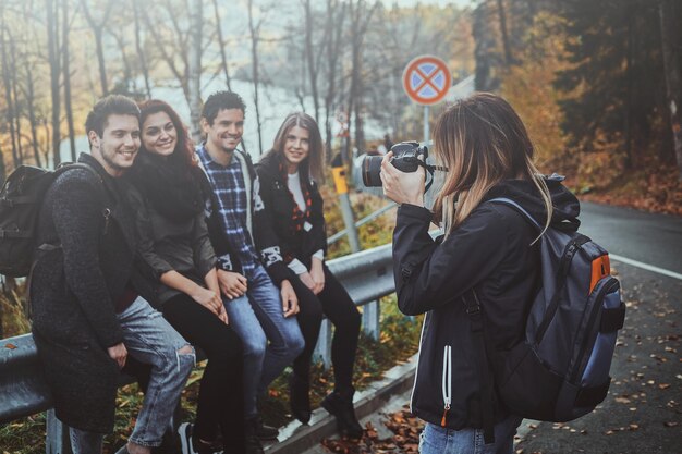 Young woman is taking a photo of her friends on digital camera at autumn forest.