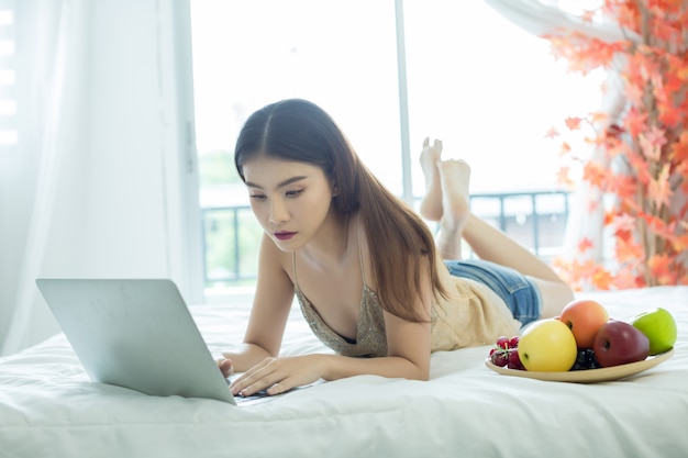 A young woman is watching a movie from a laptop on the bed at home