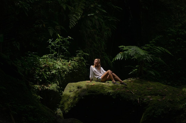 A young woman in the jungle lets out puffs of smoke Vape