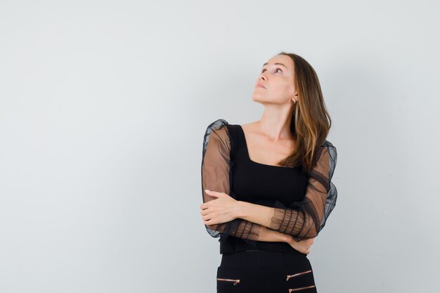 Young woman keeping arms crossed and looking left in black blouse and black pants and looking serious. front view.