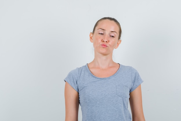 Free photo young woman keeping lips folded in grey t-shirt and looking pensive , front view.