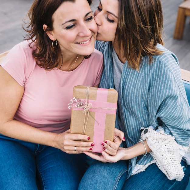 Young woman kissing adult one with gift