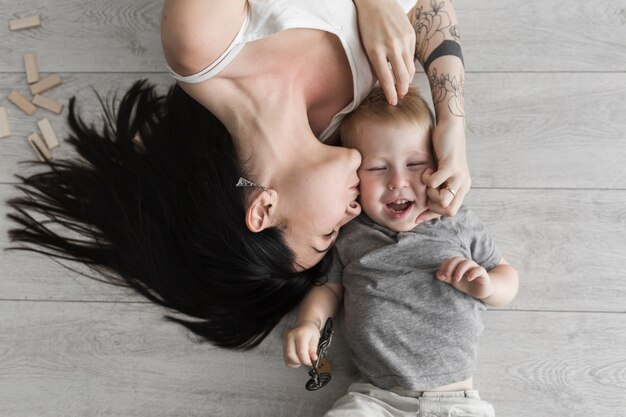 Young woman kissing her cute son lying on hardwood floor