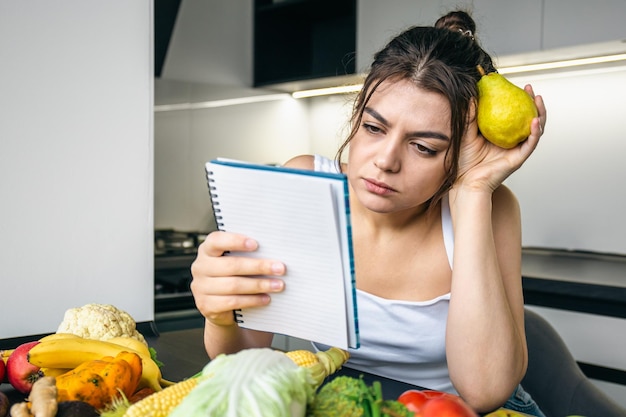 Free photo a young woman in the kitchen with a notebook among vegetables